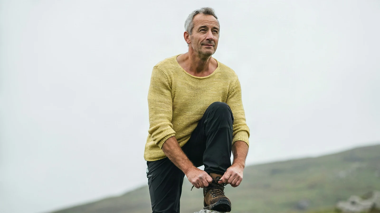 A man lacing his boots on a hillside