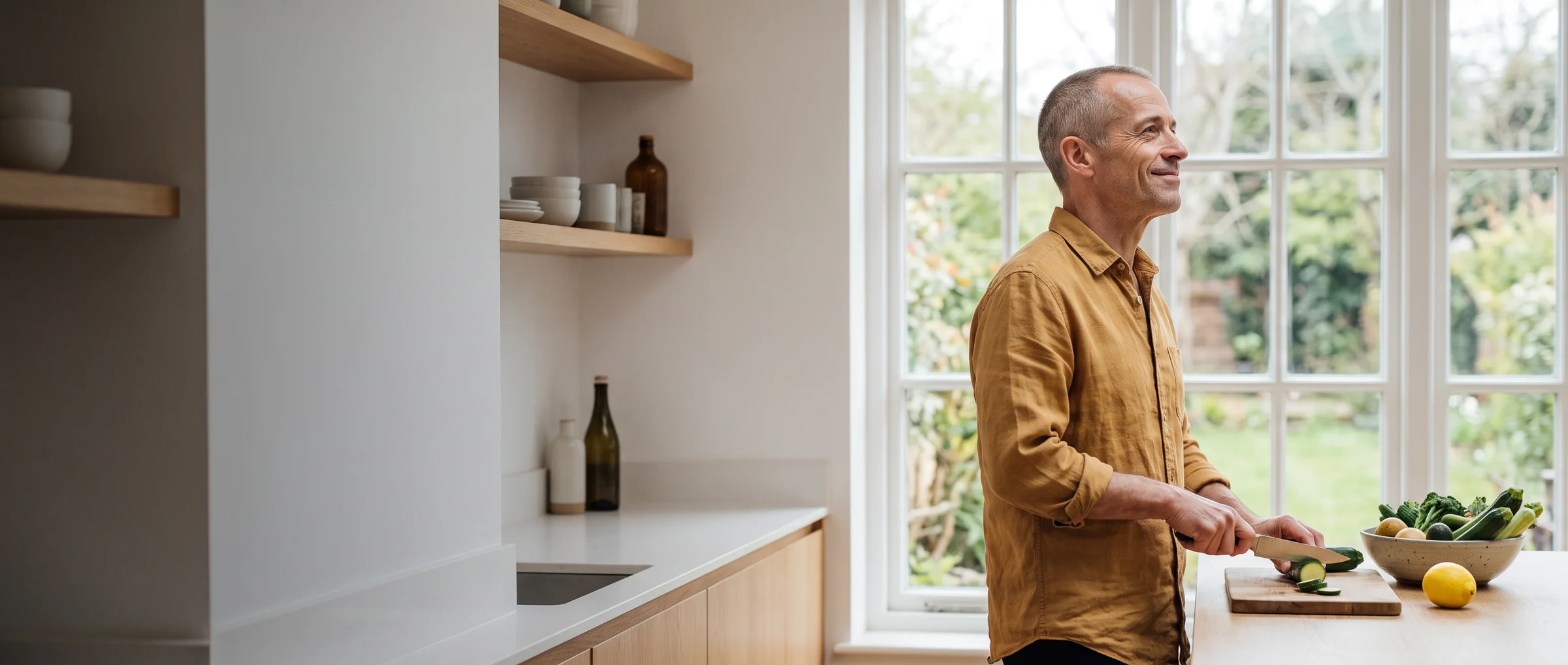 The same man at home in the kitchen, slicing vegetables by the window